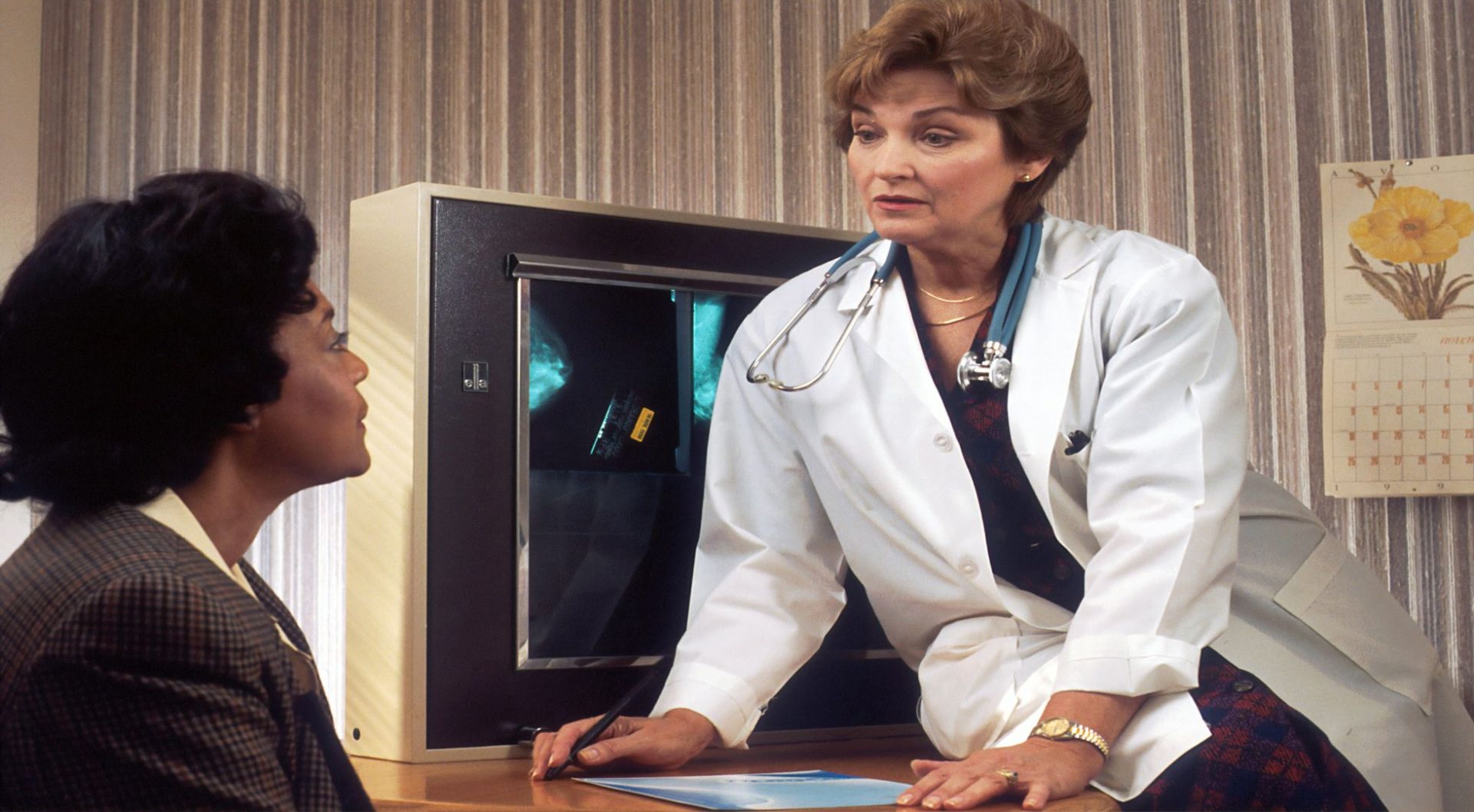 Doctor leaning on desk, speaking with patient